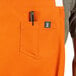 An orange Uncommon Chef bib apron with pockets holding a pen.