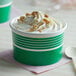 A close up of two green Choice paper cups filled with ice cream, whipped cream, and nuts.