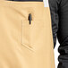 A man wearing a light beige Uncommon Chef bib apron with natural webbing and three pockets.