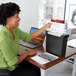 A woman sitting at a desk using a GBC ShredMaster paper shredder.