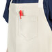 A person wearing a sand beige Uncommon Chef Vibe Bib Apron with a red pen in the pocket.