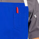 A person wearing a blue Uncommon Chef bib apron with natural webbing and red pen in a pocket.