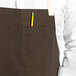 A person wearing a dark brown Uncommon Chef Vibe apron with a pencil in the pocket.