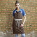 A woman wearing a dark brown Uncommon Chef Vibe bib apron with natural webbing.