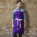 A man wearing a purple Uncommon Chef apron with natural webbing and 3 pockets.