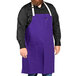 A man with a beard wearing a purple Uncommon Chef bib apron with natural webbing and 3 pockets.