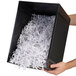 A hand holding a black box with shredded paper.