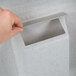 A hand using a white Koala Kare baby changing station to put a white paper in a white plastic lid.