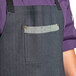 A person wearing a Uncommon Chef Zig Zag Denim Renegade Bib Apron with black webbing and 3 pockets over a purple shirt.