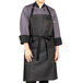 A person wearing a Uncommon Chef black denim bib apron with black webbing.