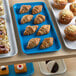 A blue Cambro market tray holding a variety of pastries and desserts.