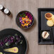 A black Front of the House porcelain bowl with food on a table.