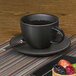 A Front of the House semi-matte black porcelain saucer with a cup of coffee and fruit on a plate.