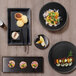 Front of the House Spiral Ink black porcelain plates with food on a table.