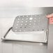 A hand holding a stainless steel metal tray with holes in the bottom.
