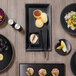 A table with Front of the House Spiral Ink semi-matte black rectangular porcelain plates of food.