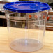 A Carlisle clear plastic food storage container with a blue lid on a wooden counter.