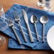 A close-up of an Acopa Phoenix stainless steel salad/dessert fork on a blue napkin.