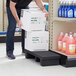 A man using a Regency black plastic display base to stack a case of soda on a table in a grocery store aisle.