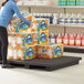 A woman using a black plastic Regency display base to hold a large box of laundry detergent on a table in a grocery store aisle.