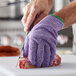 A person wearing purple San Jamar level cut resistant gloves cutting meat.