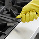 A hand in a yellow glove using a Carlisle utility brush to clean a stove.