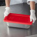 A person in gloves holding a red rectangular Vollrath steam table lid.