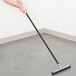 A person using a Rubbermaid Lobby Pro wet/dry cleaning wand squeegee to clean a floor.