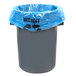 A grey garbage can with a blue plastic bag over it.
