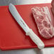 A Dexter-Russell butcher knife on a cutting board next to meat.