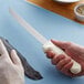A person using a Dexter-Russell Sani-Safe fillet knife to cut a fish.