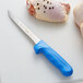 A Dexter-Russell Sani-Safe narrow boning knife with a blue handle next to a piece of chicken.