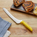 A Dexter-Russell yellow scalloped bread knife next to a sandwich on a cutting board.