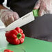 A person cutting a red pepper with a Dexter-Russell Sani-Safe green chef knife.