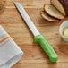 A Dexter-Russell Sani-Safe bread knife with a green handle on a wooden surface.