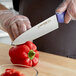 A person cutting a red bell pepper with a Dexter-Russell purple chef knife.