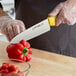 A person in a plastic glove cutting a red pepper with a Dexter-Russell yellow chef knife.