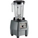 A Waring commercial food blender with a clear container, black lid, and grey base.