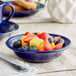 An Acopa Capri deep sea cobalt stoneware bowl filled with fruit on a table.