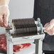 A hand using a Backyard Pro Butcher Series Jerky Slicer blade on a meat machine.