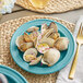 A close up of Acopa Capri Caribbean Turquoise stoneware plate with clams and onions on a table.