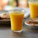 A Duralex glass of orange juice on a table with a plate of bread.