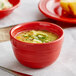 A red Acopa Capri stoneware bouillon bowl with soup on a table.