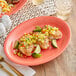 An Acopa Capri coral reef oval stoneware coupe platter with chicken, mango salsa, and lime wedges on a table.