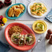An Acopa Capri coral reef oval stoneware platter on a table with plates of food, including a taco and fried shrimp.