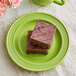 A close up of chocolate brownies on a green Acopa Capri stoneware plate.
