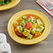 A close up of a yellow Acopa Capri stoneware plate with a salad on it and a fork.