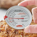 A person holding a Cooper-Atkins probe dial meat thermometer over a pizza.