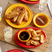 A table with Acopa Capri mango orange stoneware plates of fried spring rolls, dumplings, and food with a glass of water.