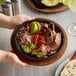 A person holding a plate of sizzling meat and vegetables with tortillas on a wooden surface.